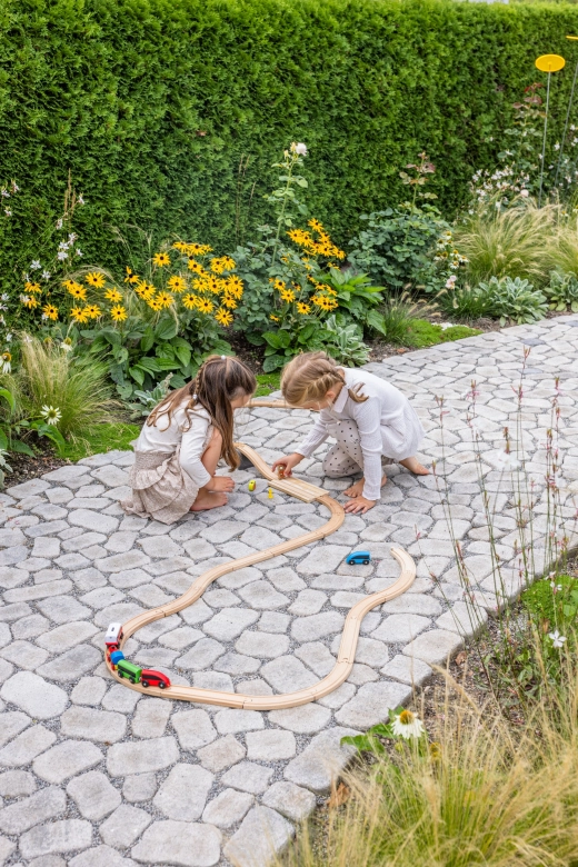 Zwei Kinder spielen mit einer Holzeisenbahn auf einem Gartenweg mit GDM.BOLERO stone.