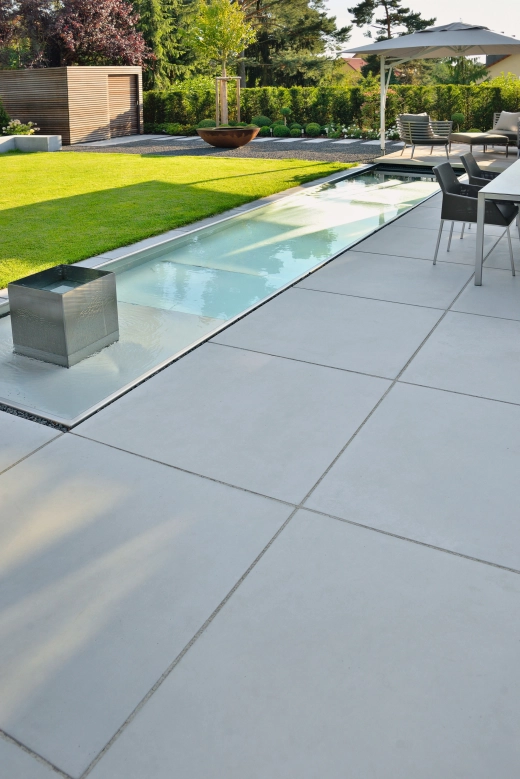 moderner linearer Garten mit großformatigen Platten aus Sichtbeton und dekorativem Wasserbecken.