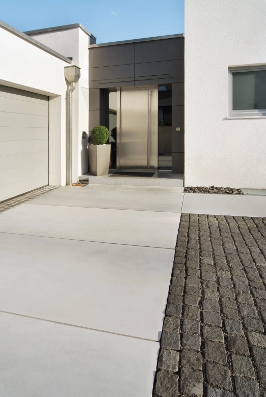 <span>zwei Meter breite, graue Sichtbetonplatten vor einem modernem und minimalistischem Hauseingang mit anthrazit verkleideter Fasade und weißm Haus.</span>