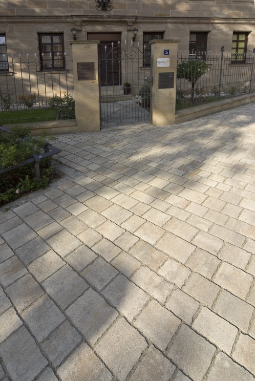 mit Naturstein gepflasterter Platz vor einem Eingang mit zwei Säulen aus Sandstein und einem geschmiedetem Gusseisenzaun.