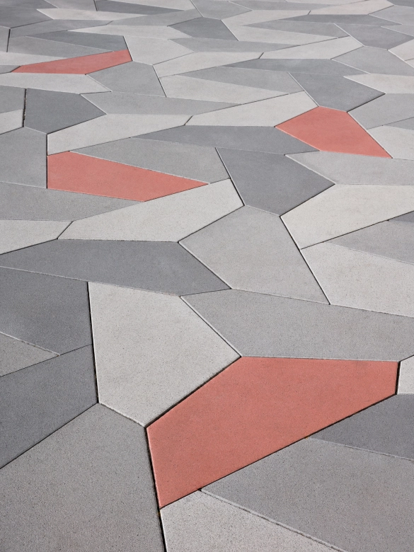 <span>fünfeckige Platten aus Beton in drei Grautönen und rot in einem geometrischen  Verlegemuster angeordnet.</span>