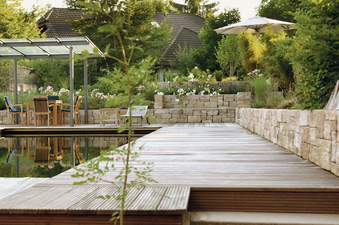 Natürlicher Garten mit Schwimmteich von einer natürlichen Mauer umgegeben 