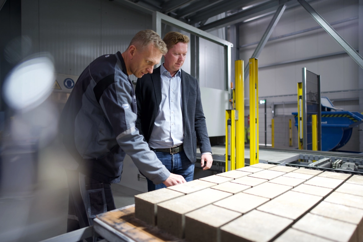 Freshly produced concrete stone layer from the machine being inspected by two people.