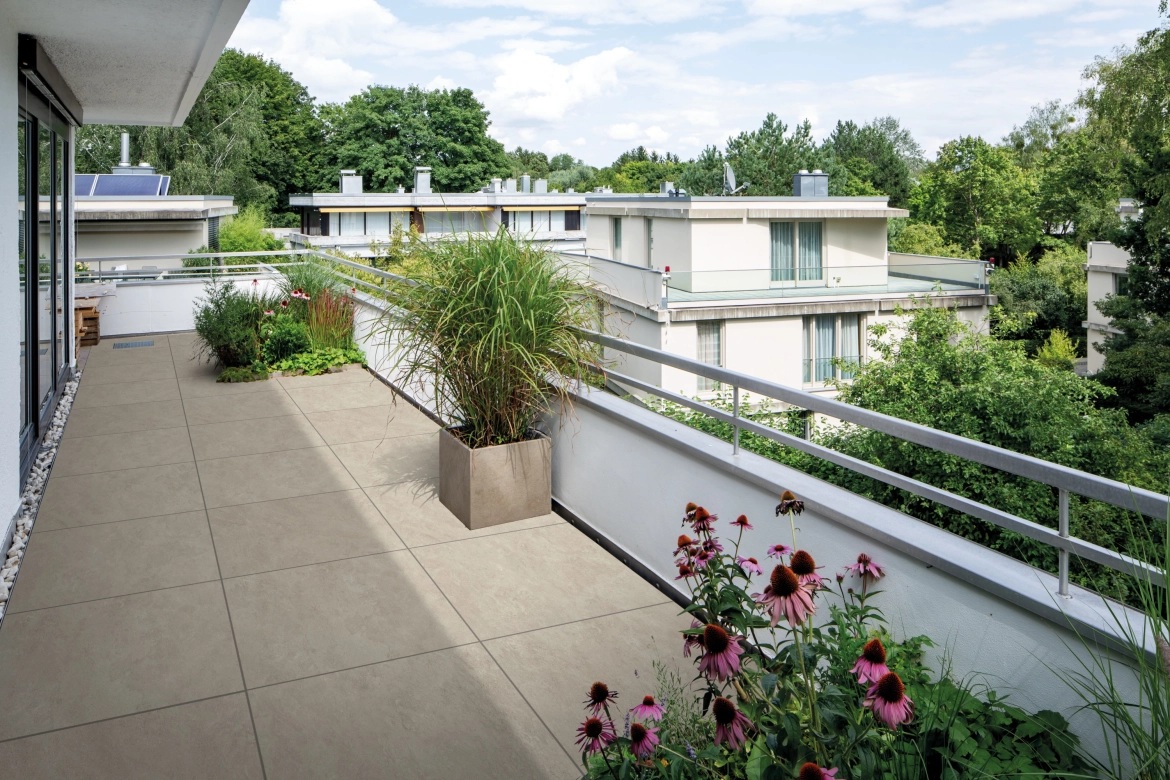 Große Dachterrasse bestückt mit vielen Pflanzen- und Blumentöpfen und den Keramikverbundplatten GDM.LIVA twice, bietet eine gute Aussicht auf ein modernes Wohngebiet inmitten vieler grüner Bäume.