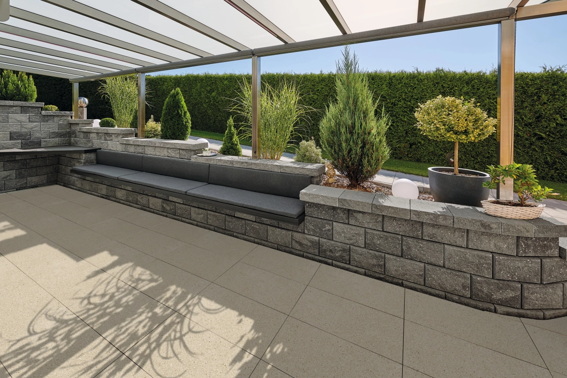 Eine Terrasse mit Dach, Mauer und Hecke im Hintergrund