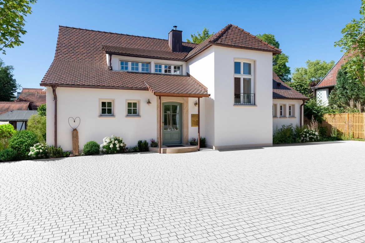 sanierter Altbau mit weißer Fassade und rot gedecktem Sattel-Walmdach. 
Der Hof ist mit hellem Granit Naturstein im Reihenverband gepflastert.