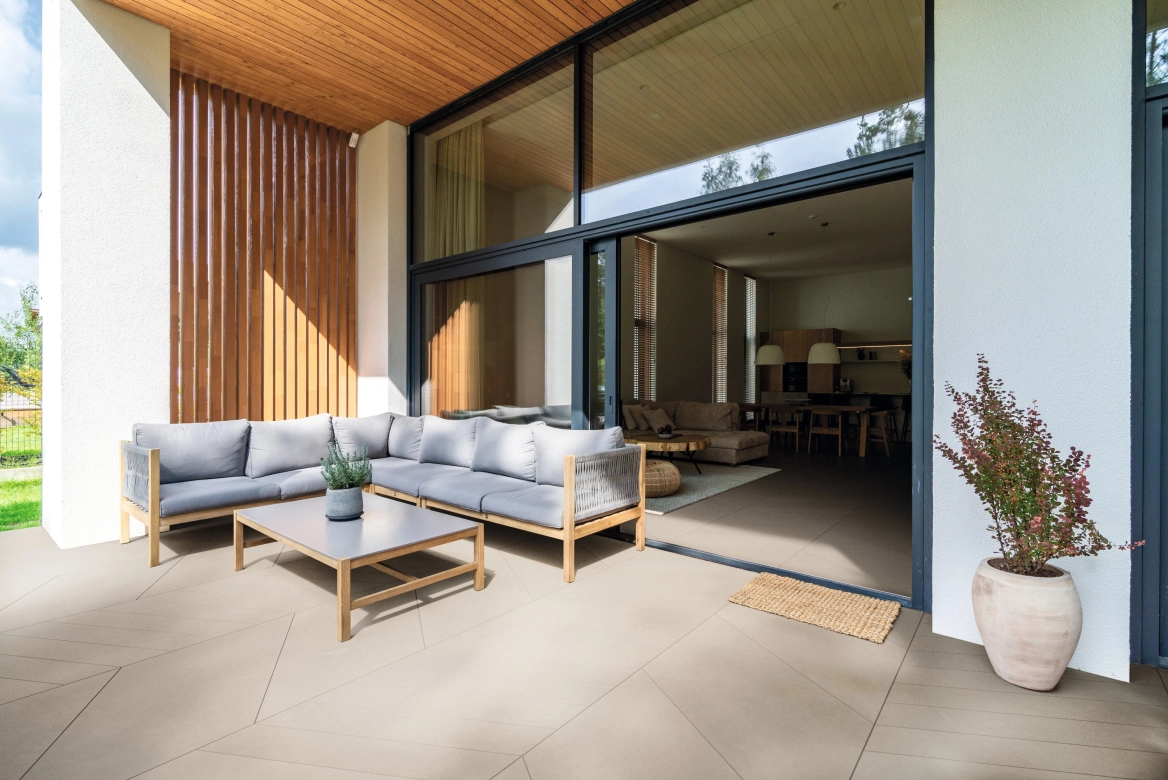 Terrasse mit Outdoor-Couch und Blick in das Wohnzimmer. Terrasse und Wohnzimmer wurden mit AWA tile belegt, wodurch in fließender Übergang zwischen innen und außen entsteht.