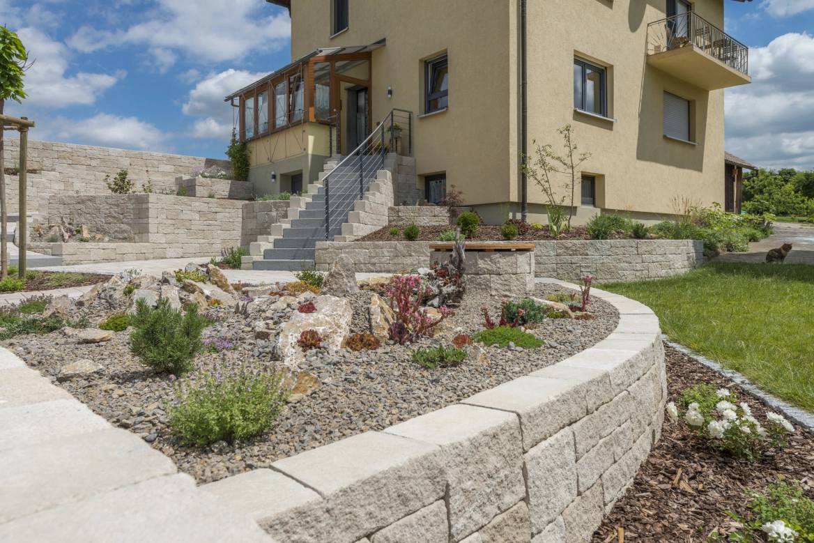 Sanierter Altbau mit beiger Fassade und neu angelegtem, terrassiertem 
Garten, großem Treppenaufgang aus Naturstein in Sandgrau und 
Beeteinfassungen aus Kalkstein Mauersteinen.<br>