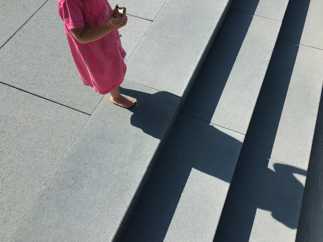 Mädchen mit rosa Kleid steht auf grauen Terrassenplatten und grauen Stufen