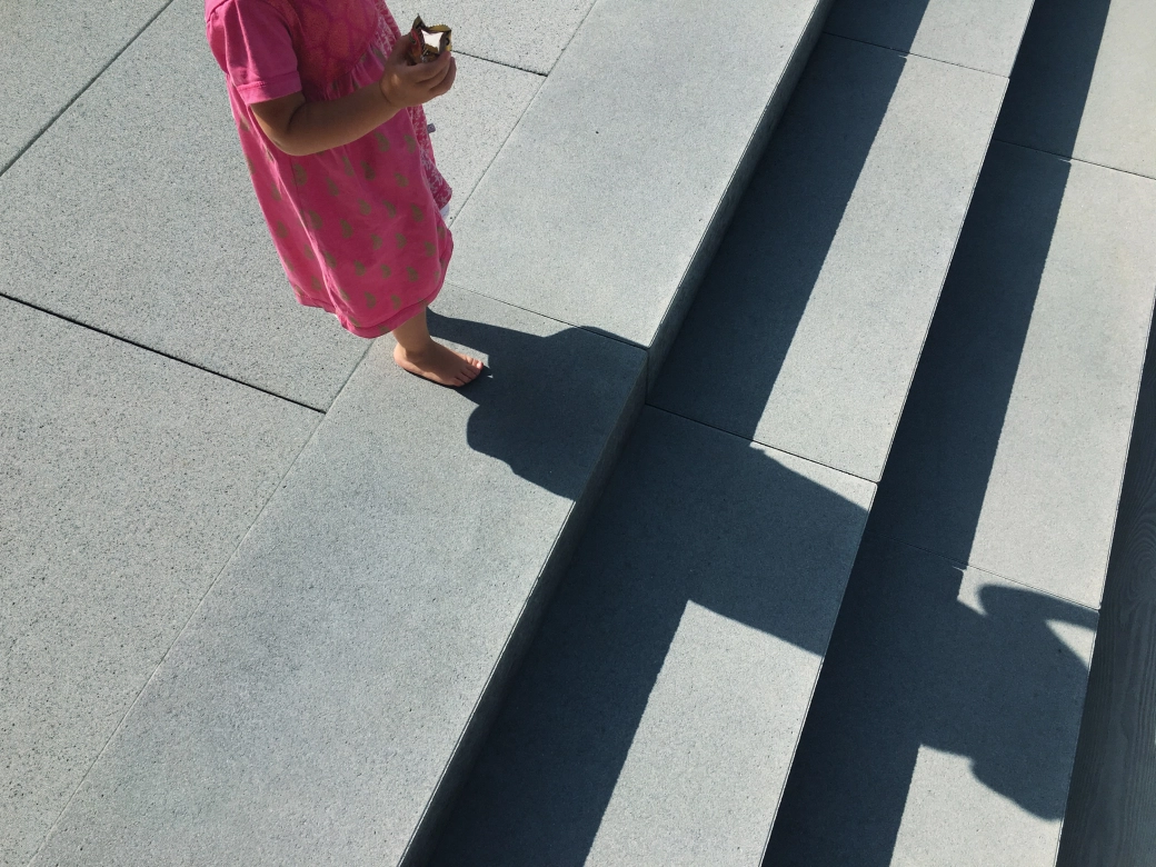 Girl with pink dress stands on gray patio tiles and gray steps