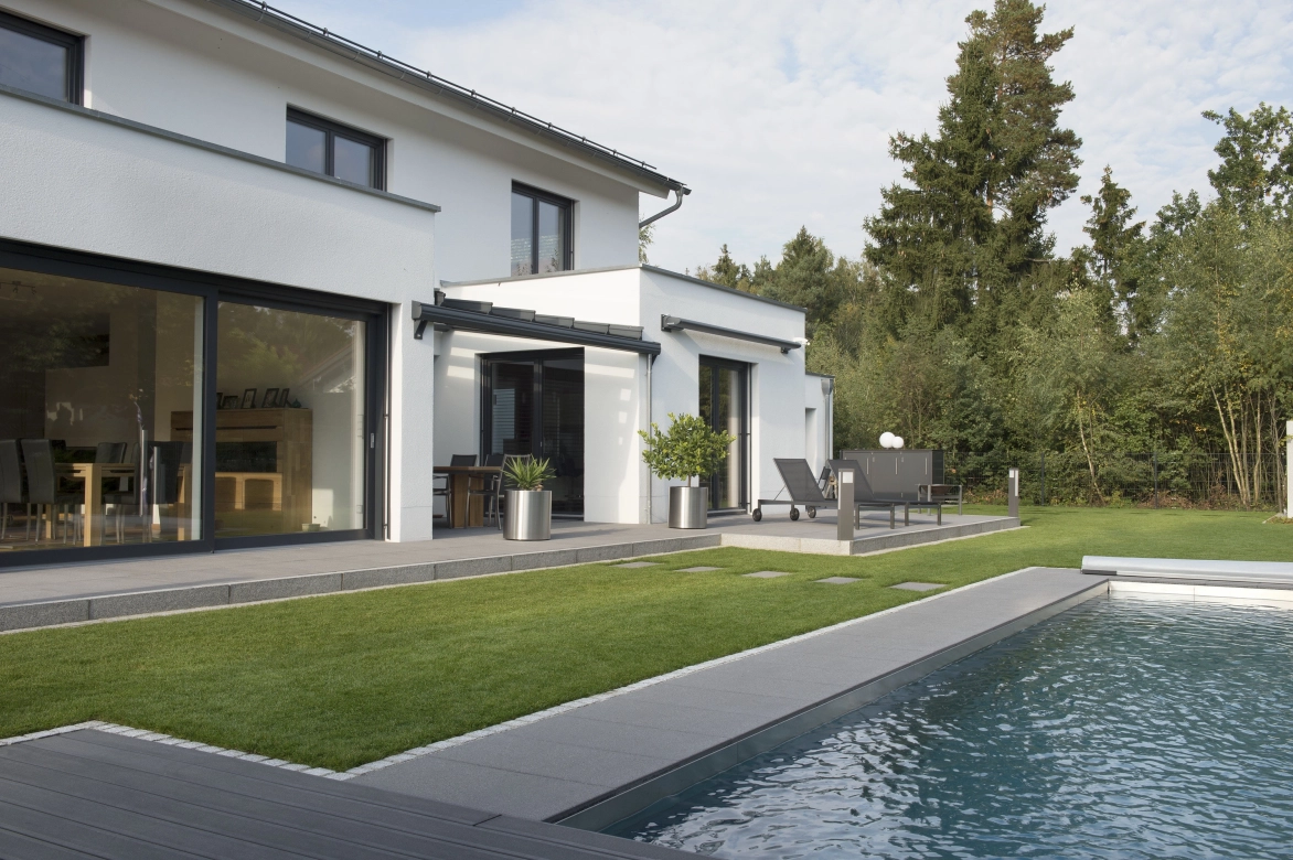 geradliniger Pool mit Betonplatten vor einem großzügigen Haus mit Glasfront 