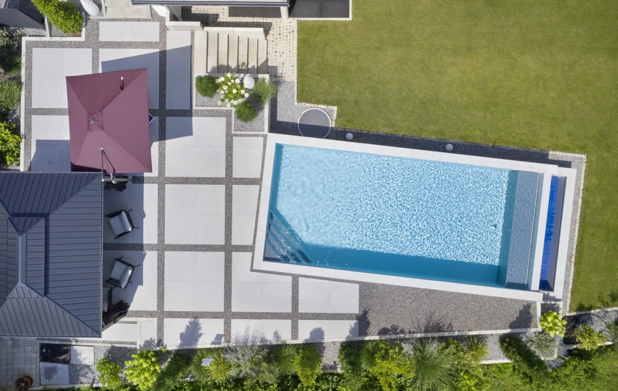 Garten mit Pool aus der Vogelperspektive, vier großformatige, quadratisch angelegte Terrassenplatten strukturieren den Außenbereich und schaffen eine moderne, großzügige Optik