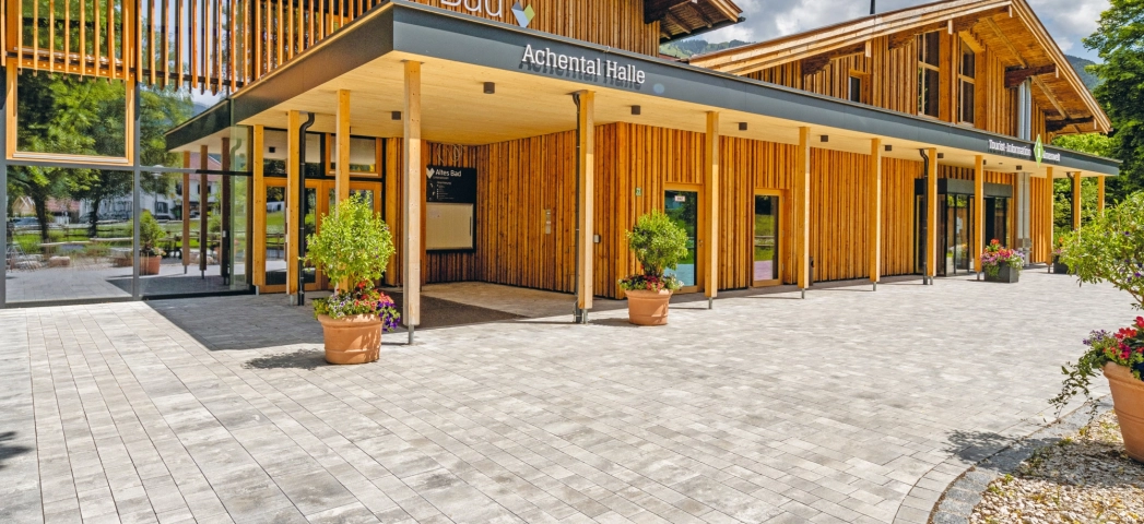 Modern gepflasterter Platz mit  Grünfläche und Sitzelementen vor einem Bürgerzentrum  mit Holzfassade