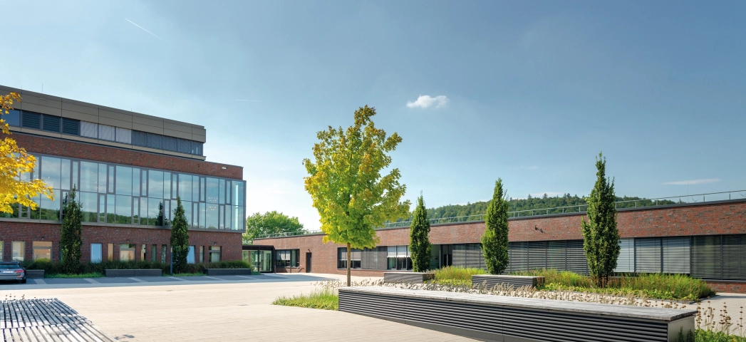 moderne Weggestaltung hin zu Unternehmensgebäude mit hölzernen Sitzgelegenheiten und sandfarbenen Pflastersteinen