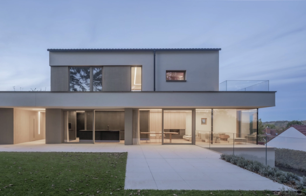 Abendliche Aufnahme eines hell beleuchteten, modernen Wohnhauses. Im Vordergrund ist ein gepflegter Rasen und eine große Terrasse zu erkennen.