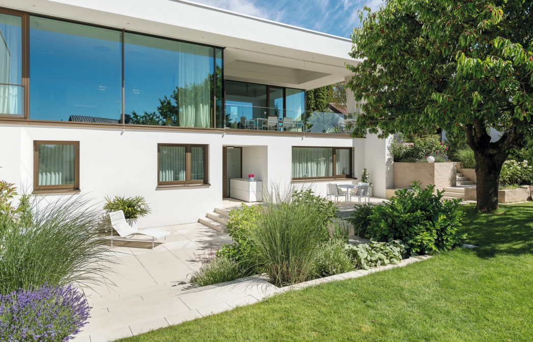 Private modern garden with sandstone-colored terrace and lots of greenery