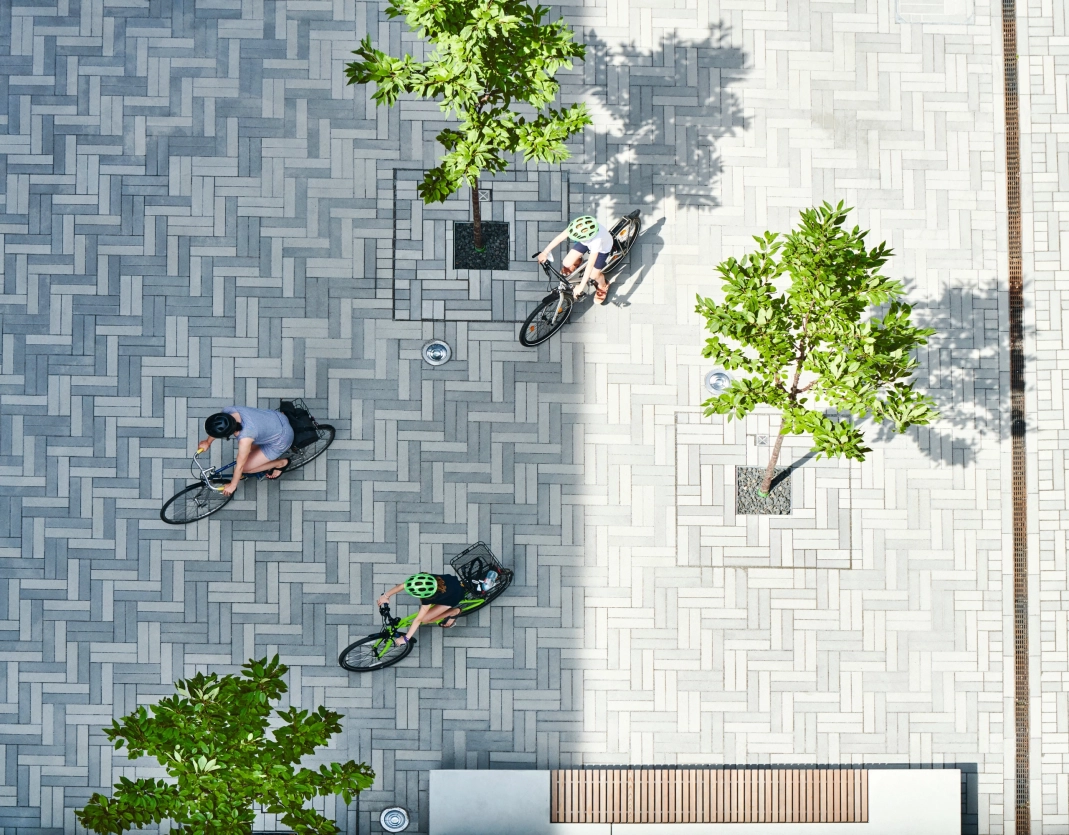 Luftbildaufnahme: Drei Radfahrer sind auf einer Flläche mit GDM.SCADA stone im schlanken Riemchenformat, das imi Fischgrätverband verlegt wurde, in grauen Abstufungen zu sehen.