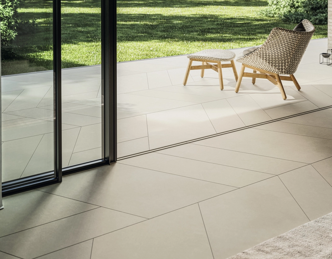 Blick vom Wohnzimmer auf die Terrasse: GDM.AWA tile - die feine Betonfliese in sanftem Beigeton, schafft einen fließenden Übergang von Innen nach Außen.