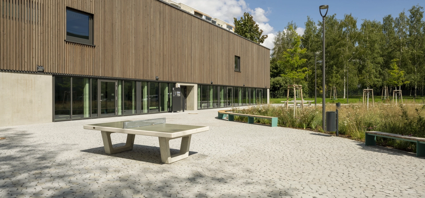 Vorplatz der Grundschule mit natürlichem Ökopflaster GDM.BOLERO stone auf dem eine Tischtennisplatte steht. Im Hintergrund eine natürliche Wiese und ein Wald.