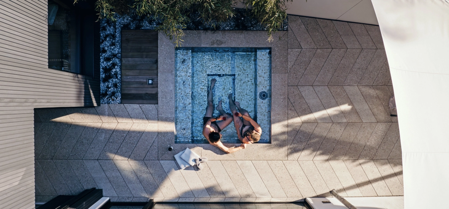 Vogelperspektive auf eine Terrasse in Fischgrätverband. Im kleinen Whirlpool sitzen zwei Menschen. Der Bodenbelag ist GDM.AWA tile von GODELMANN und im Ellbogen bzw. Fischgrätverband verlegt.