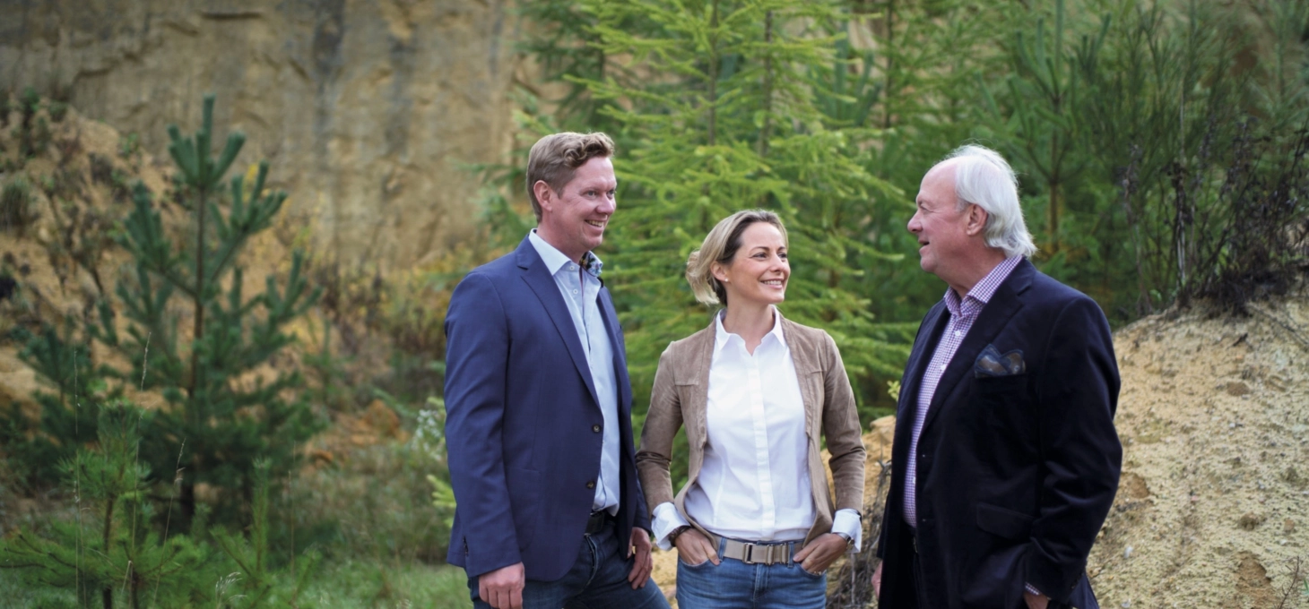 Die Geschäftsleitung von GODELMANN, Bernhard Silvia und Bernhard senior, stehen vor einen bewachsenen Sandstein-Wand.