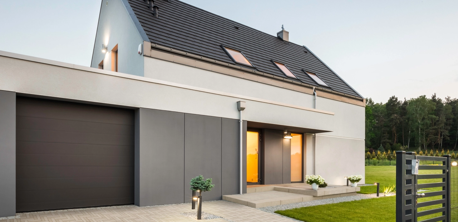 Haus mit Garage und Hofeinfahrt. Die Beleuchtung des Hauses ist angeschaltet.