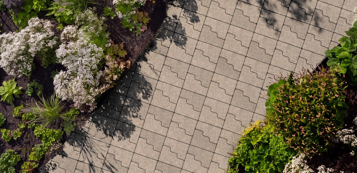 Ein mit GDM.CASCADE stone gepflasterter Weg aus der Vogelperspektive. Umrandet mit grünen und weiß blühenden Pflanzen.