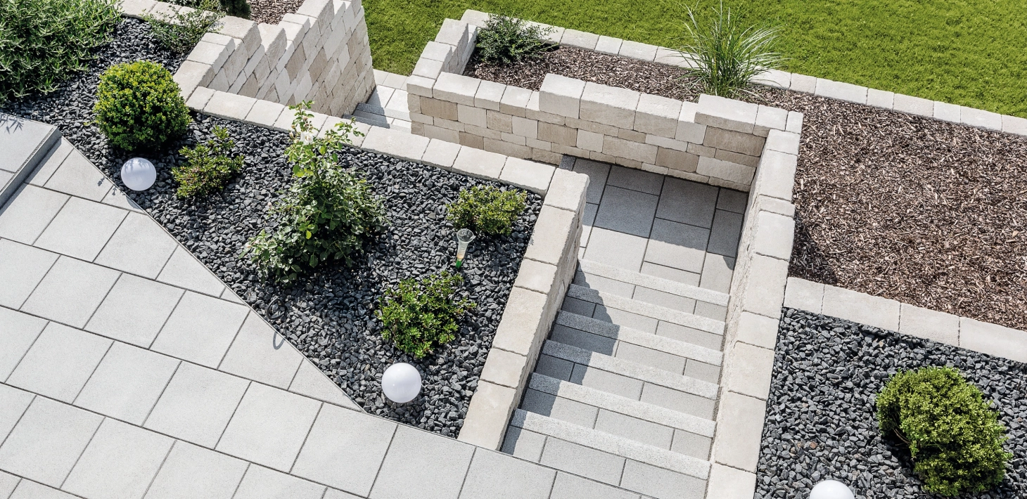 Terrasse mit Treppenabgang aus Betonstein und Terrasiertem Hang abgestützt mit einer Naturstein mauer  und angelegten udn bepflanzten Beeten.<br>