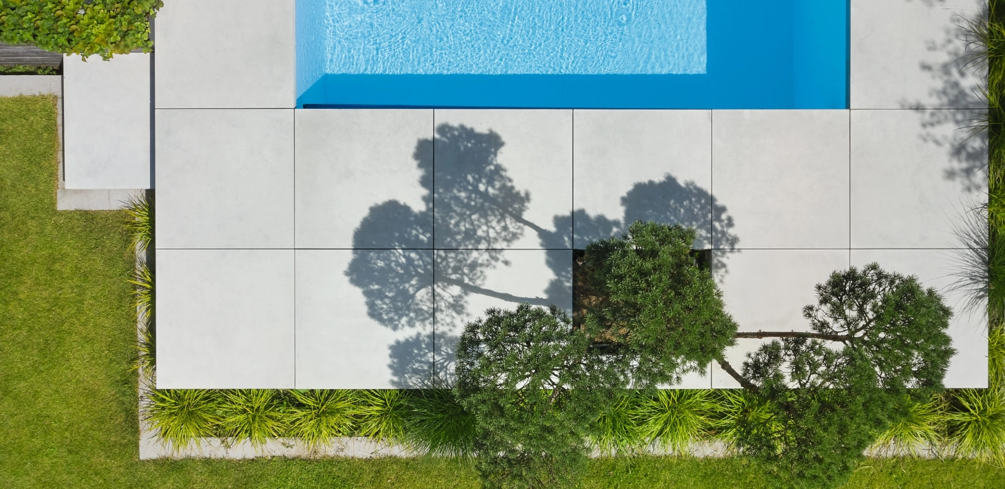 freischwebend und erhöht gesetzte Platten aus Sichtbeton in 100 x 100 cm um einen modernen Pool mit integrierter Bepflanzung.