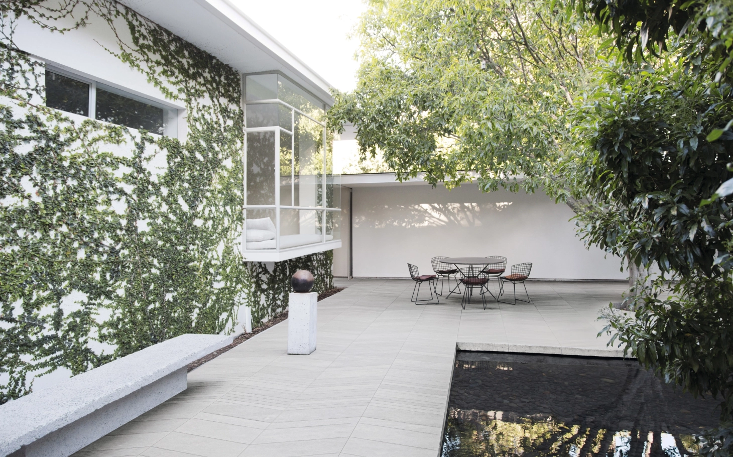 Grüner Innenhof mit moderner Sitzgelegenheit im Hintergrund und GDM.AWA tile auf dem Boden. Rechts vor der Sitzrunde befindet sich ein natürlicher Pool. 