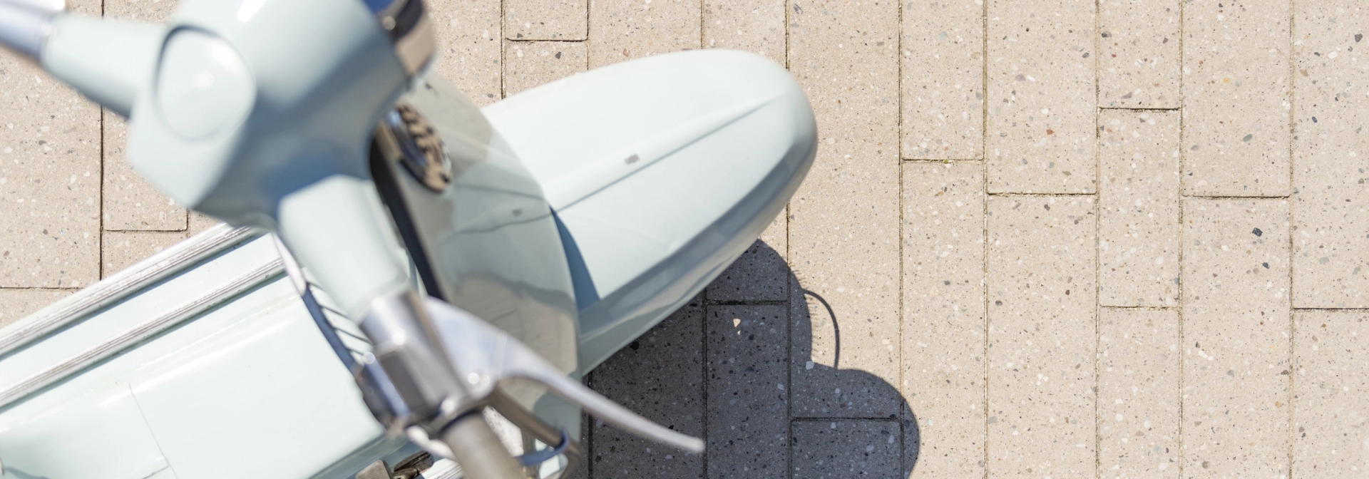 Draufischt auf eine himmelblaue Vespa auf einer geplasterten Fläche mit 
Terrazzo-Steinen mit sichtbarer Körnung Format eines Stabparkets.