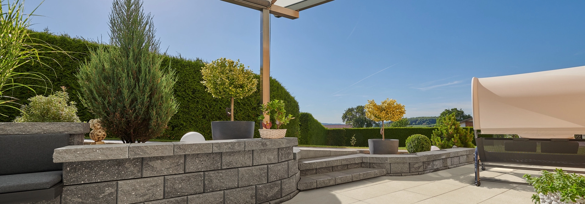 Eine Terrasse mit Dach, Mauer und Hecke im Hintergrund