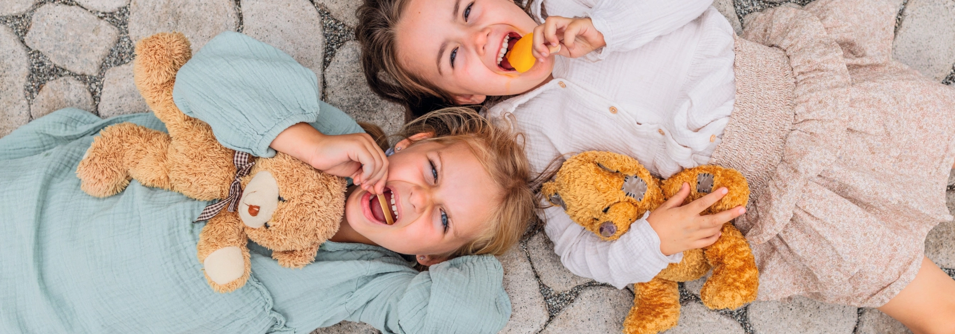Zwei Kinder liegen auf dem Gartenweg und schlecken Eis