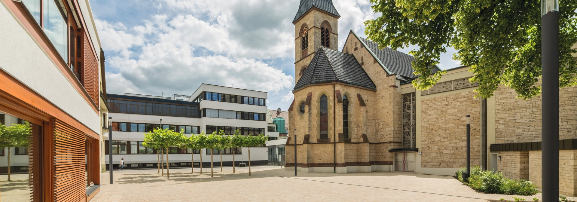 gepflasterter Kirchenvorplatz mit modernen Gebäuden und historischer Kirche