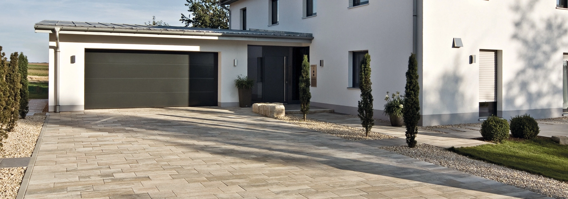 Hofeinfahrt eines Einfamilienhauses mit Garage und Pflanzen auf einem Privatgrundstück.