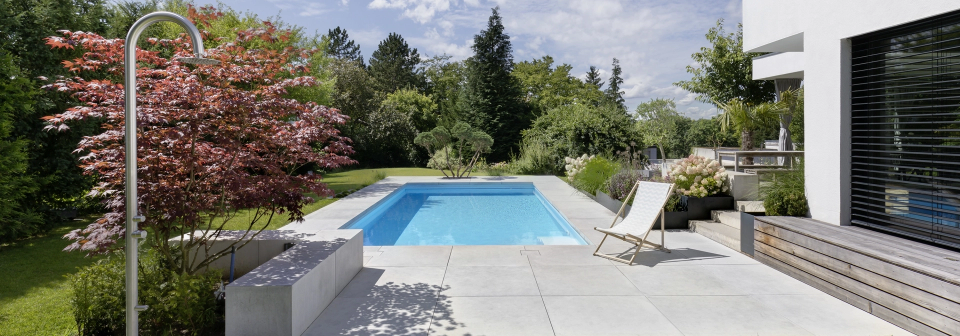 Begrünter Garten mit Pool und großformatigen Terrassenplatten auf einem Privatgrundstück.