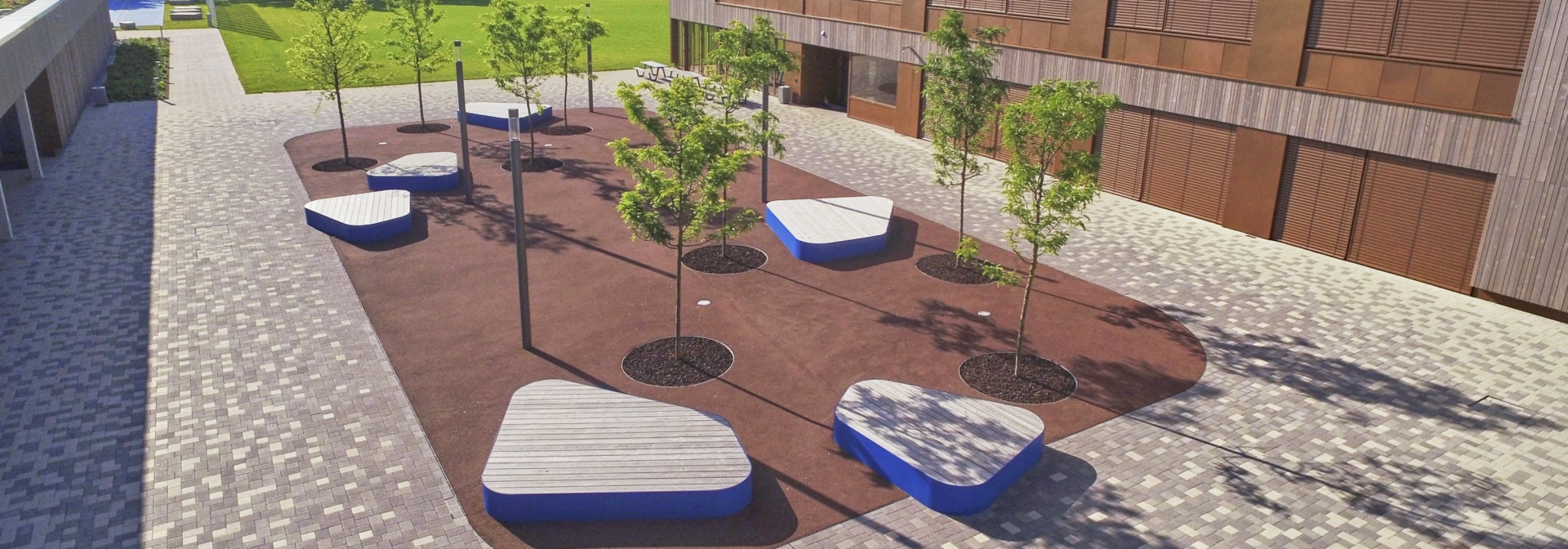 Luftbild mit Blick in den modernen Schulhof: Von hellem bis zu dunklem Braun – drei harmonisch aufeinander abgestimmte Farbtöne setzen die Freianlagen der Realschule Hirschaid im Landkreis Bamberg wirkungsvoll in Szene.