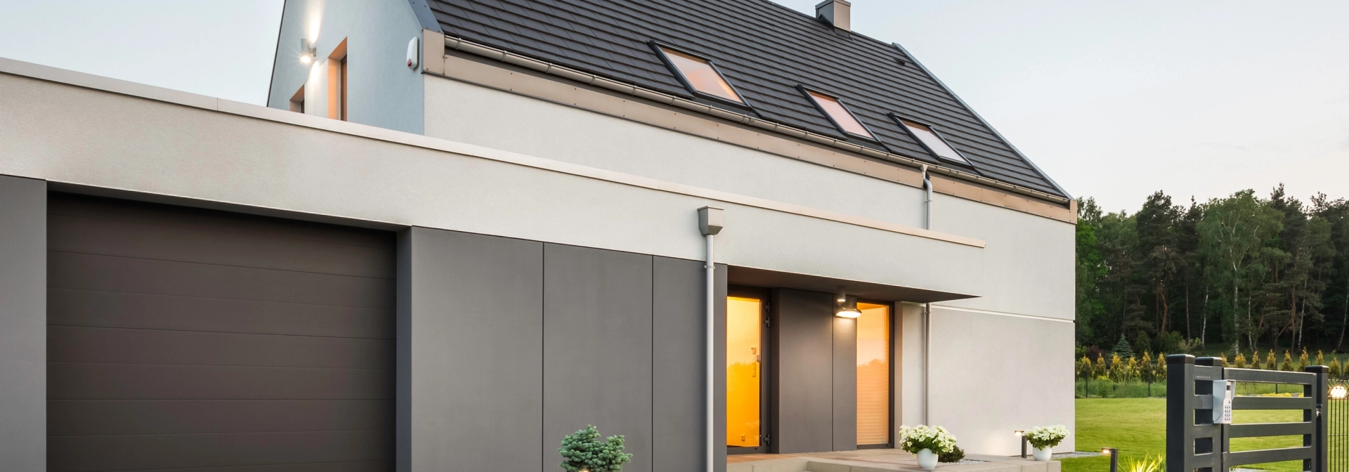 Haus mit Garage und Hofeinfahrt. Die Beleuchtung des Hauses ist angeschaltet.