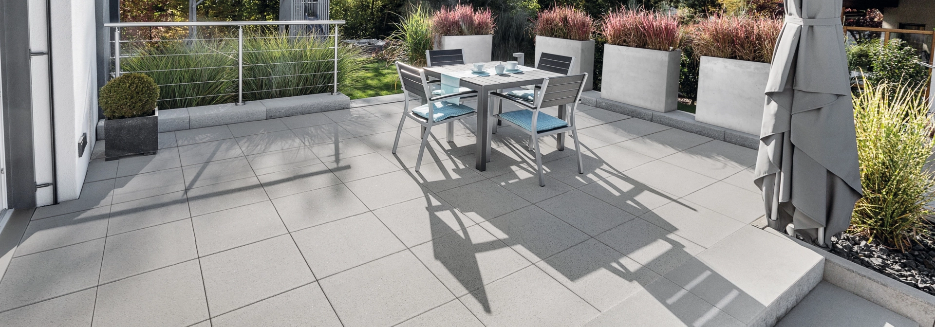 Großflächige Terrasse mit grauen Terrassenplatten und Stufen umgeben von Pflanzgefäßen.