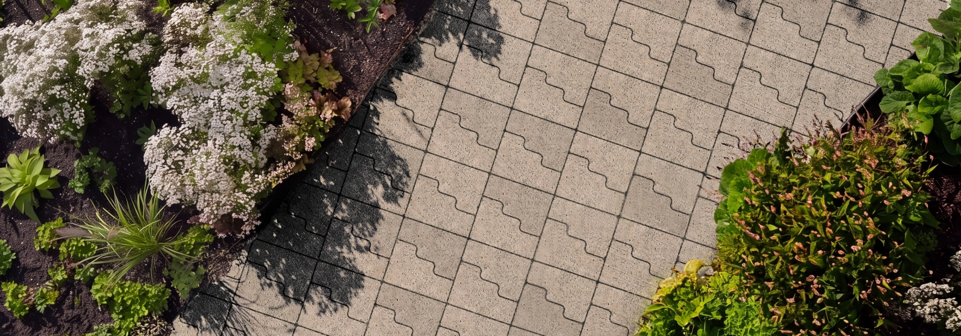 Ein mit GDM.CASCADE stone gepflasterter Weg aus der Vogelperspektive. Umrandet mit grünen und weiß blühenden Pflanzen.
