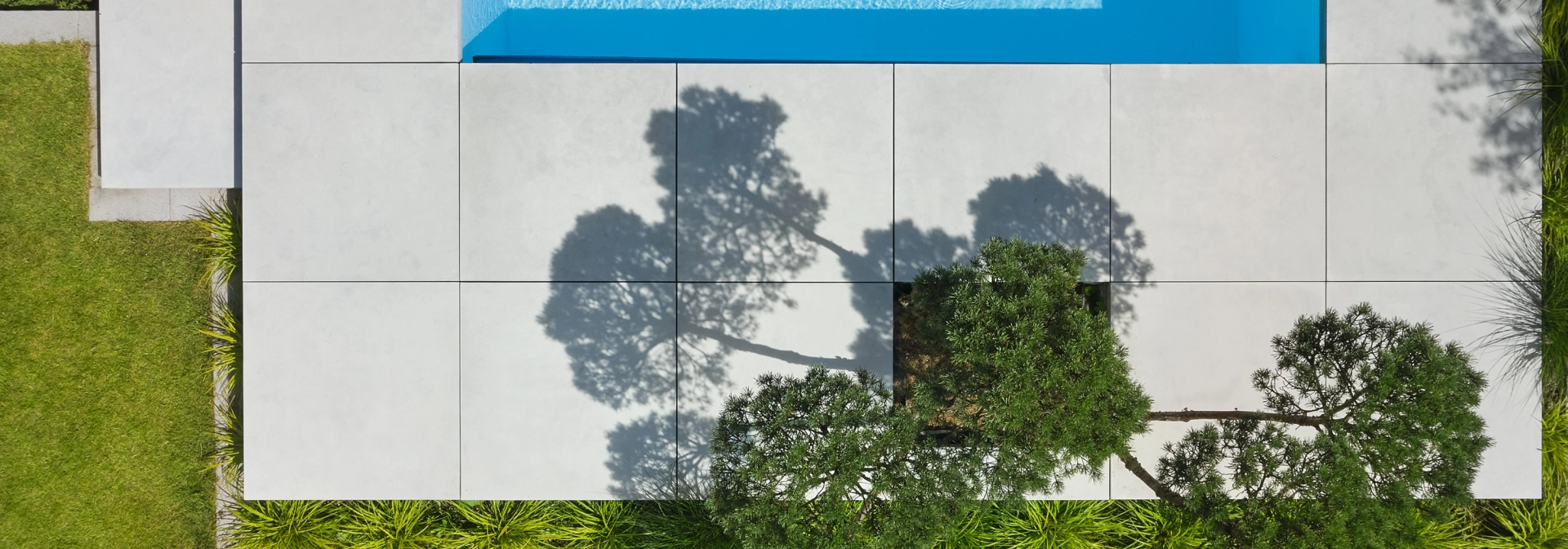 freischwebend und erhöht gesetzte Platten aus Sichtbeton in 100 x 100 cm um einen modernen Pool mit integrierter Bepflanzung.