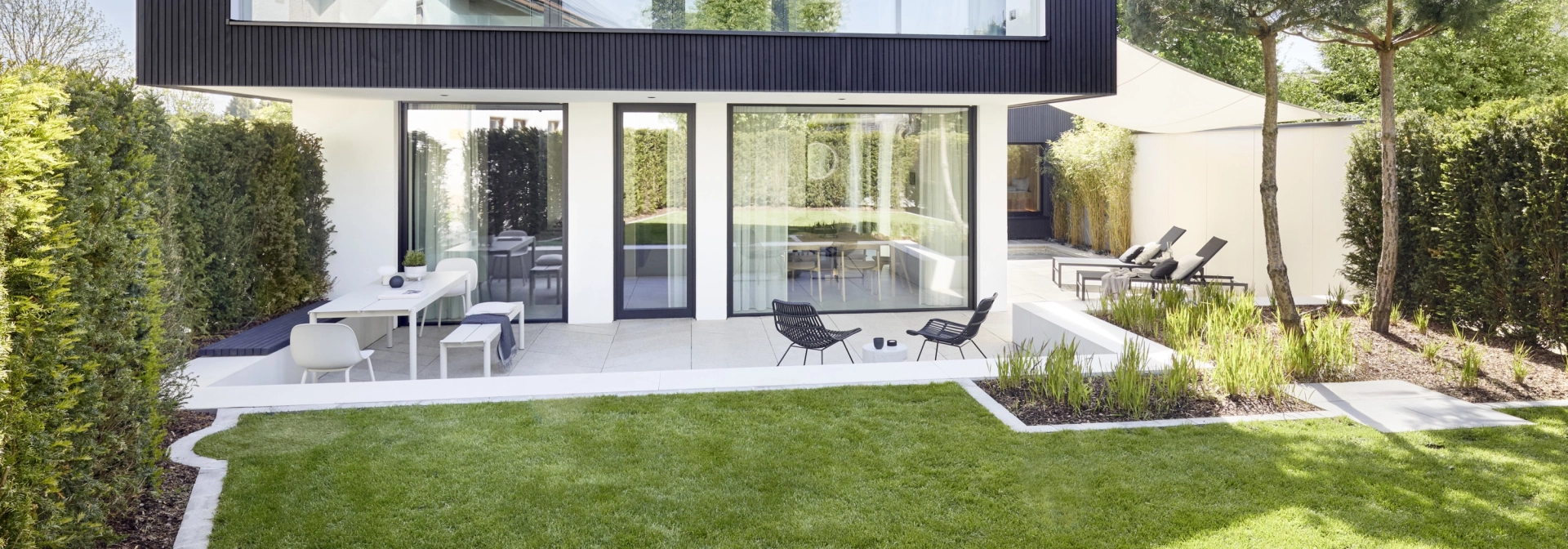 Feine Designfliesen aus Beton in Fischgräten-Optik, für die Gestaltung im Innen- und Außenbereich, sowie für die Wand und dem Boden, in einem modernen zweistöckiges Haus mit großflächigen Glasfenstern mit Terrasse, Whirlpool und Liegefläche