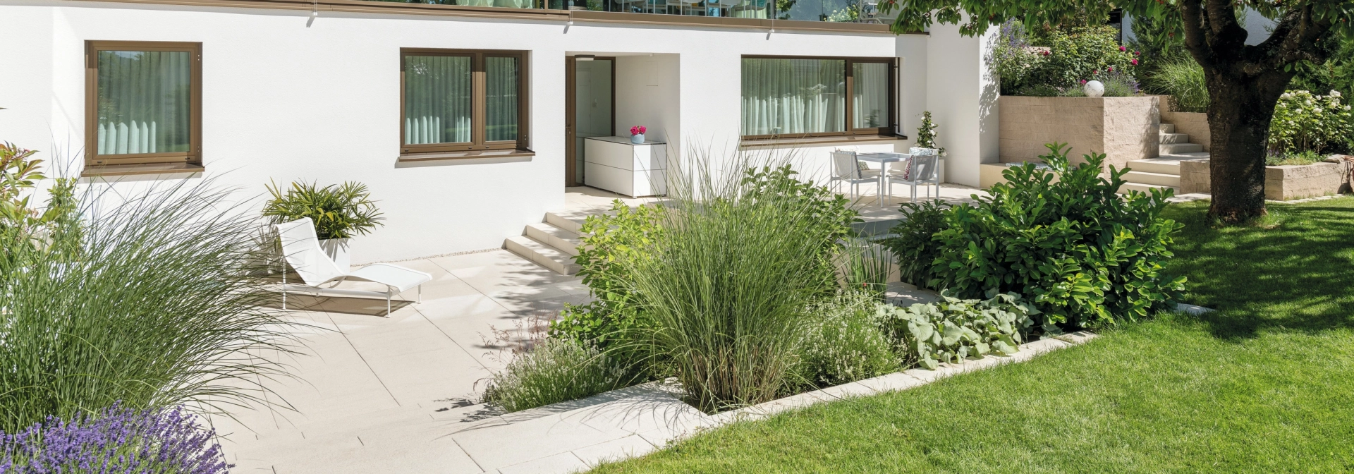 Privater moderner Garten mit sandsteinfarbener Terrasse und viel Grün