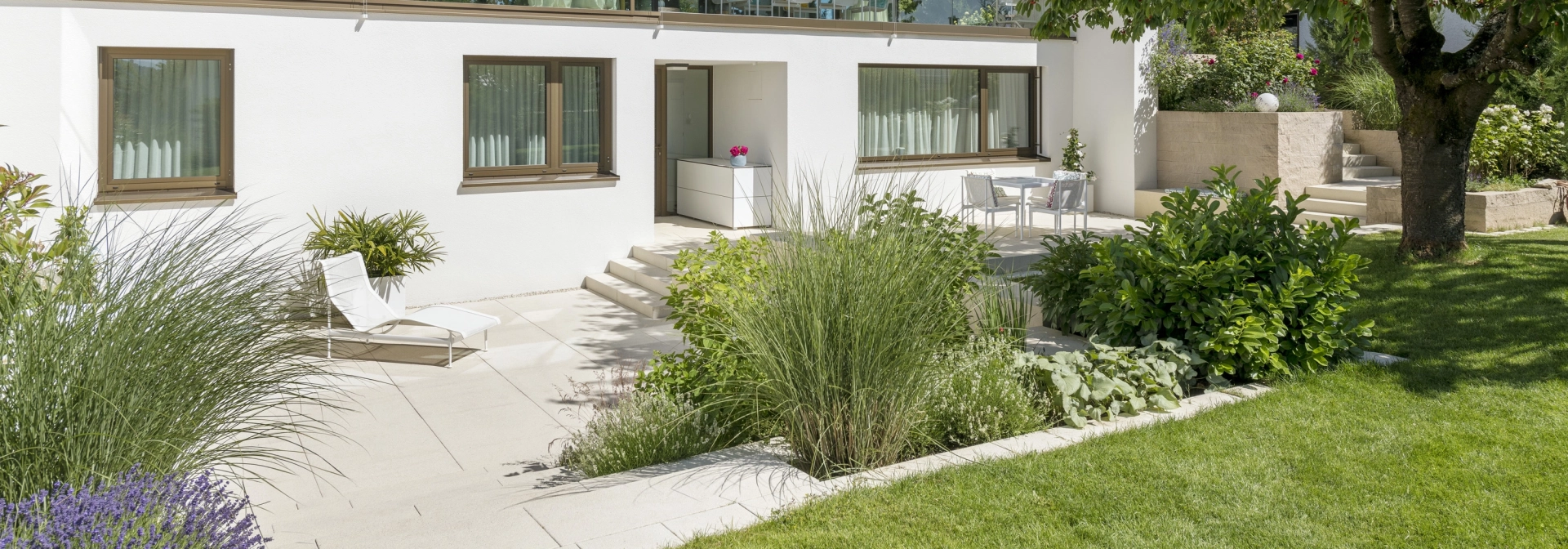 Private modern garden with sandstone-colored terrace and lots of greenery