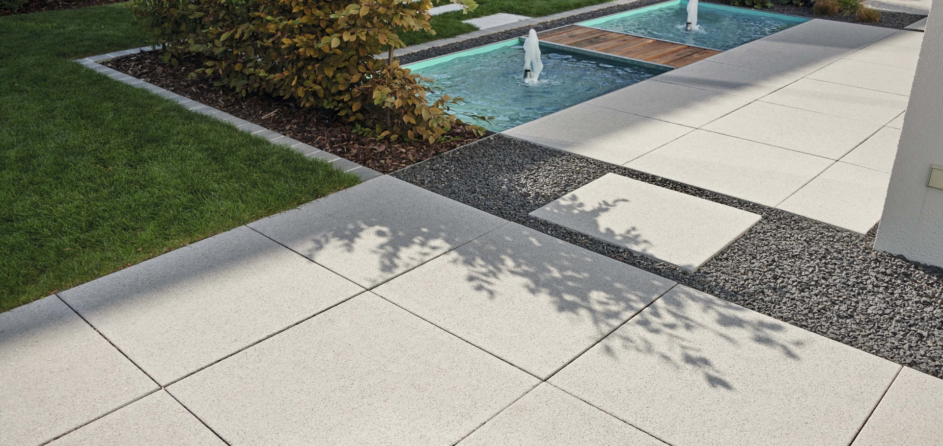 Modern garden with square large-format slabs in light gray and water basin with fountain