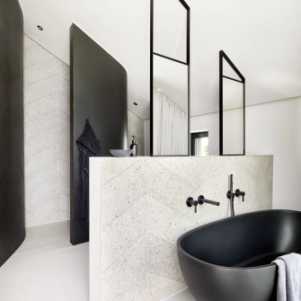 Badezimmer mit GDM.AWA tile Fliesen an zwei Wänden und freihstehender schwarzen Badewanne.