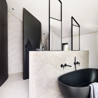 Badezimmer mit GDM.AWA tile Fliesen an zwei Wänden und freihstehender schwarzen Badewanne.