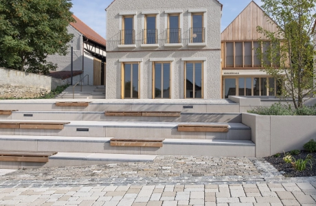 Modernes Haus mit Satteldach neben einem älteren Gebäude, mit einem ökologischen Flächenbelag im Vordergrund.