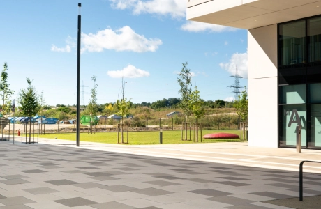 Moderner Platz auf einem Universitätscampus neben einem mehrstöckigen Gebäude mit großzügiger Freifläche, Grünanlagen und Sicht auf die Umgebung, wobei der Platz mit GDM.SCENIC stone gepflastert ist.