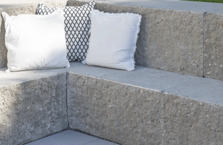 Nahaufnahme eine Sitzmöglichkeit aus granitfarbenem GDM.MAXI block. Davor sind GDM.NUEVA light verlegt und im Hintergrund ist eine Rasenfläche.